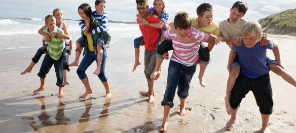 Kids piggybacking along beach on school camp