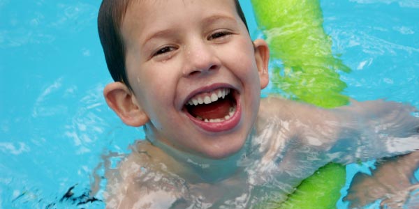 smiling boy at school swimming lessons learning to swim with noodle